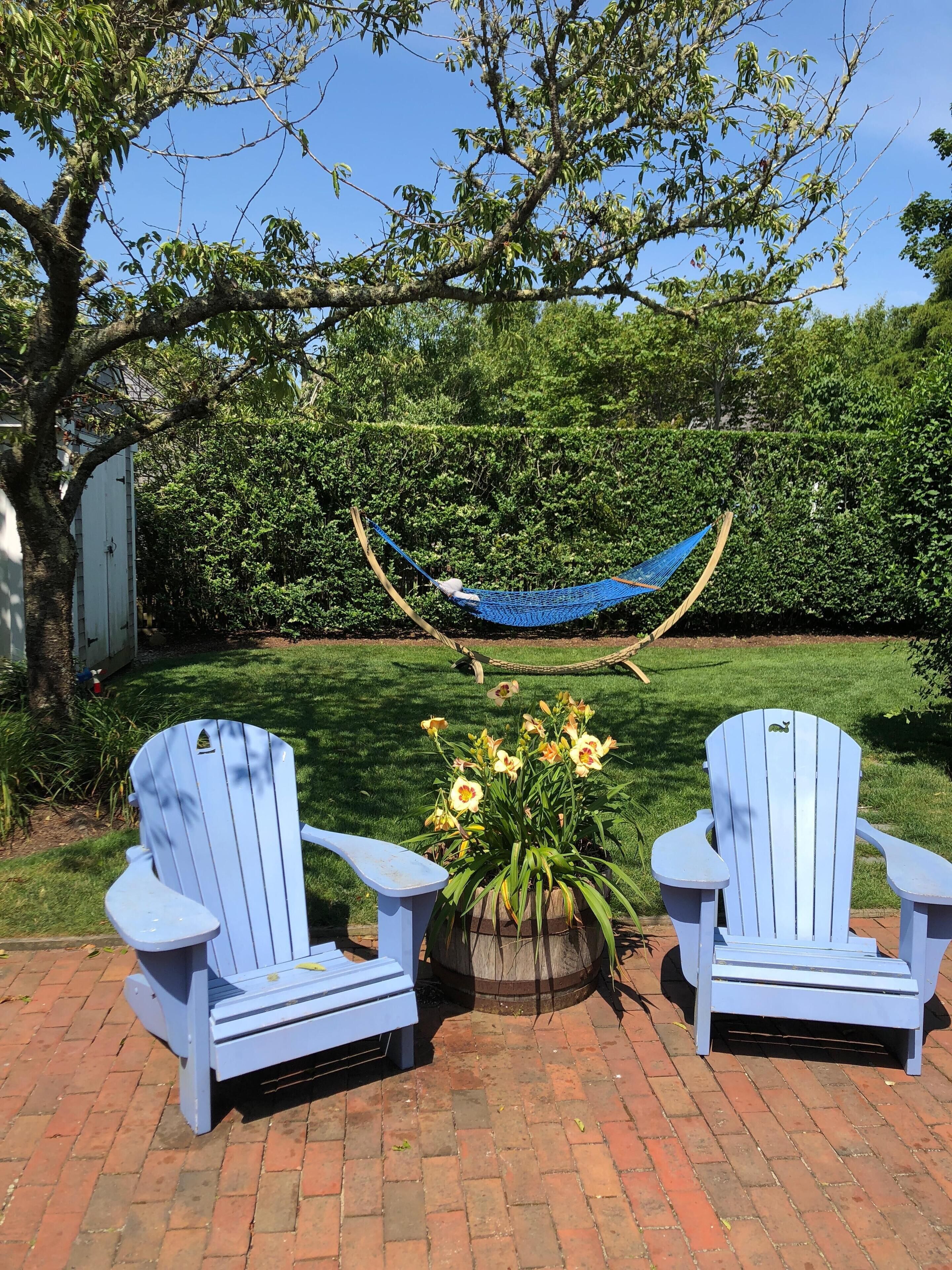 Zwei Adirondack-Stühle, eine Hängematte und eine Blumenanordnung in einem Garten.