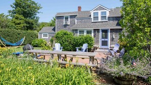 A two-story house with a front porch, a hammock, and a picnic table with chairs. - Ten min. walk to Main St. Perfect for families/groups. Gorgeous enclosed yard. (Nantucket)