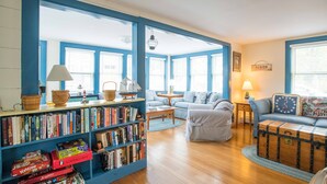 A cozy living room with a bookshelf, a sofa set, a wooden coffee table, and a decorative trunk. - Ten min. walk to Main St. Perfect for families/groups. Gorgeous enclosed yard. (Nantucket)