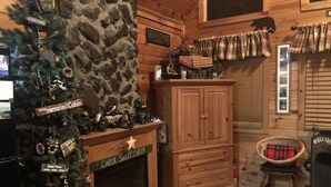 Un acogedor interior de cabaña con chimenea de piedra, un árbol de Navidad y un armario de madera.