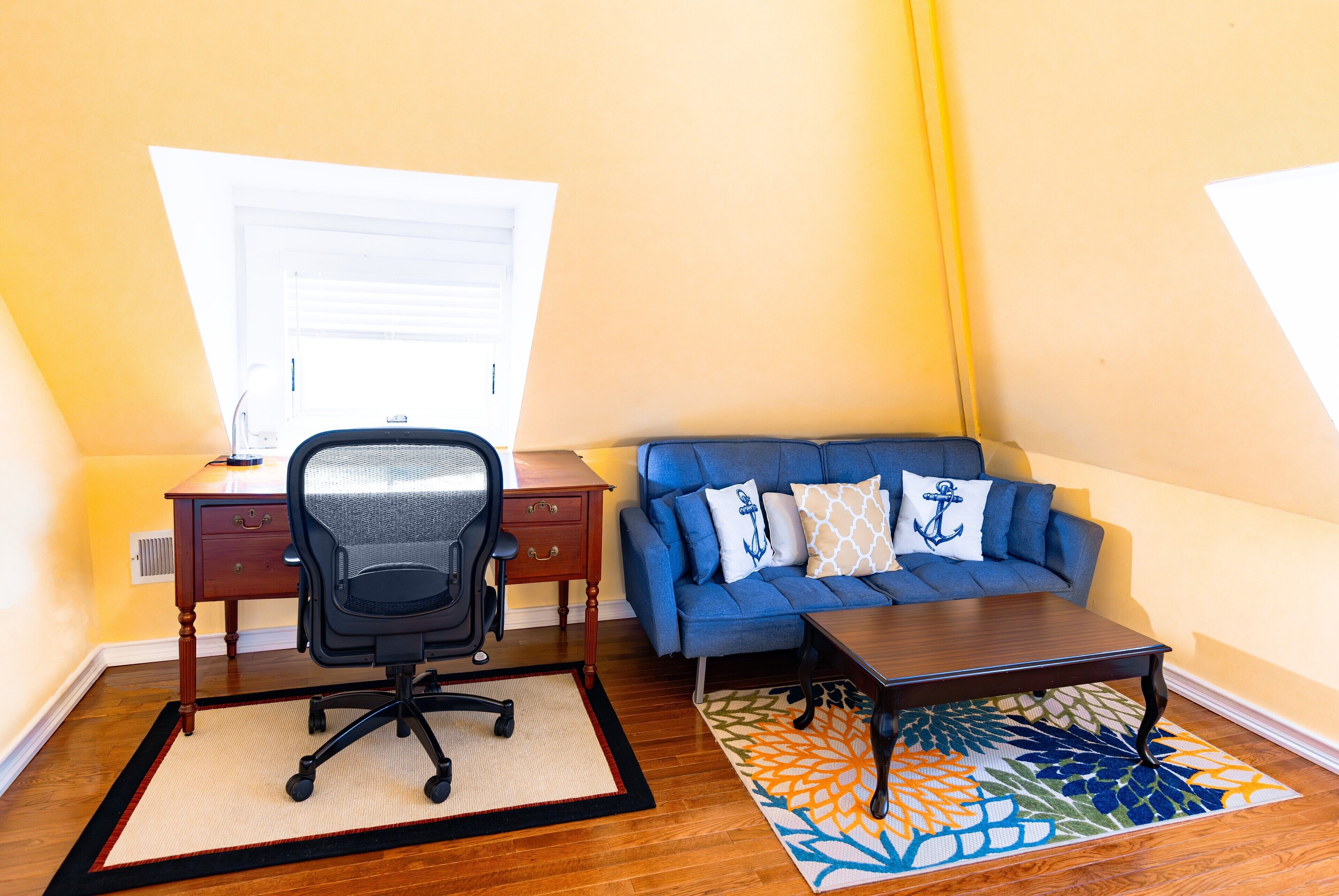 Una habitación con escritorio, silla, sofá y una pequeña mesa.