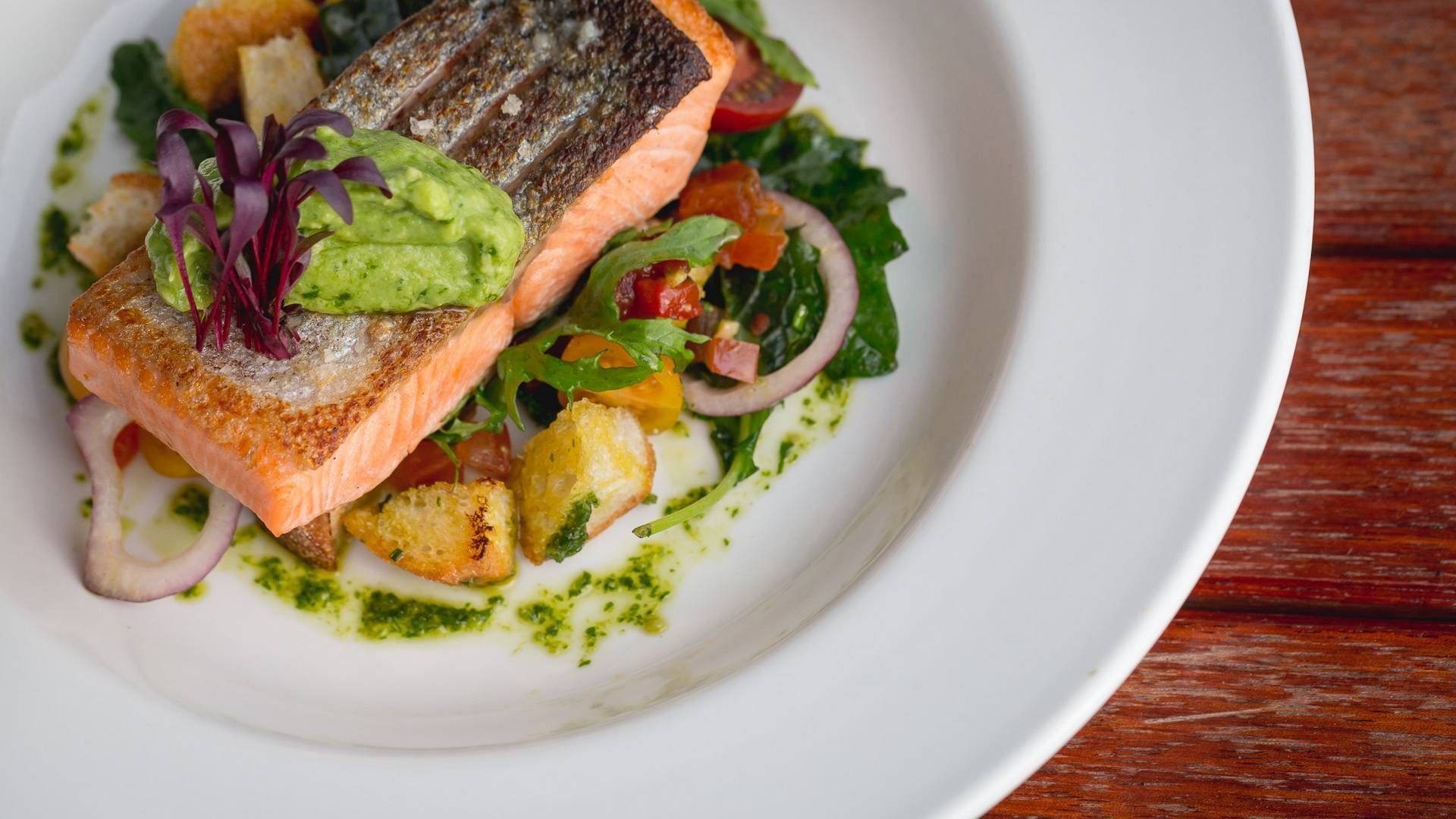 Une assiette de nourriture comprenant du saumon, de l’avocat et des légumes.