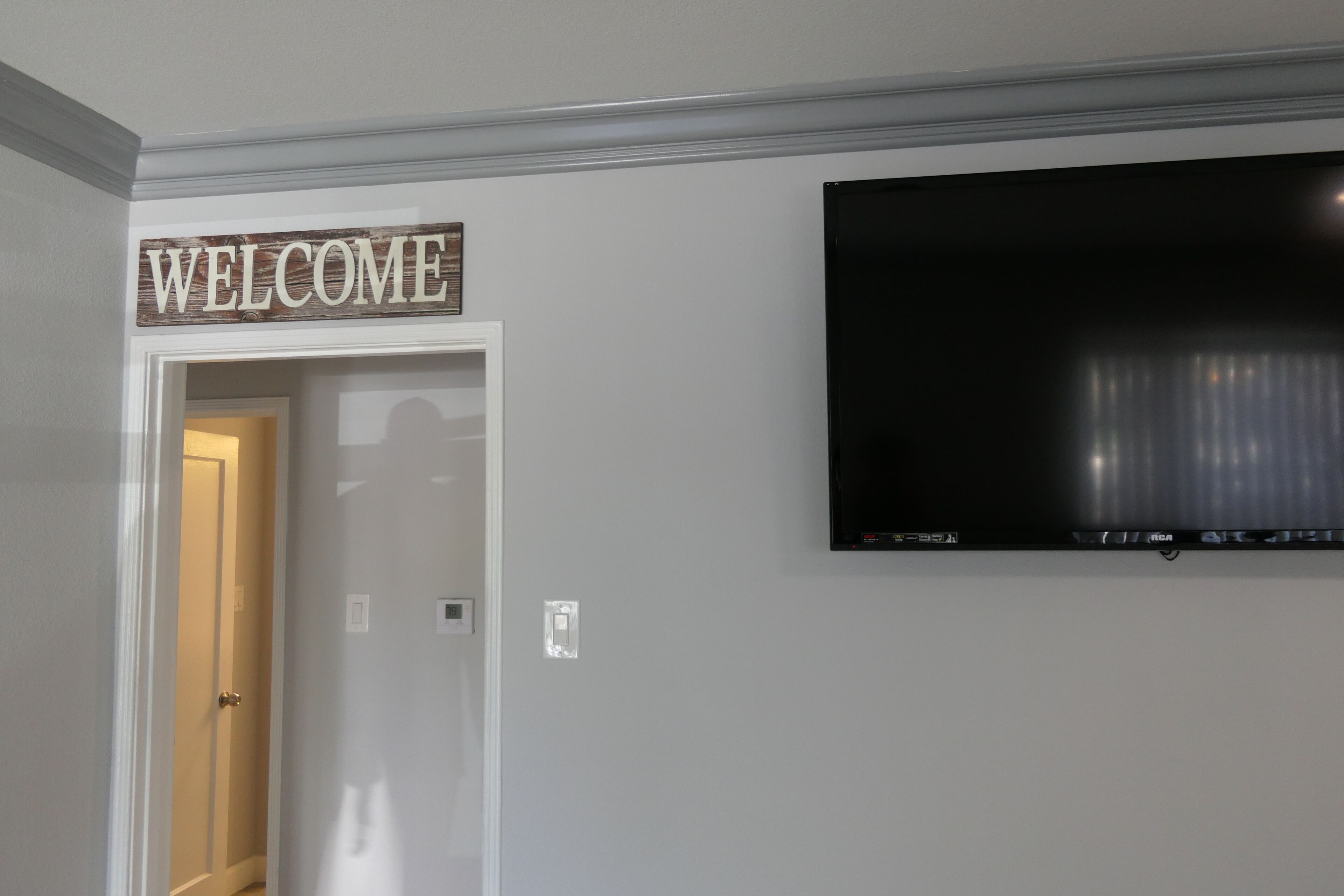 Una habitación con un cartel que dice 'WELCOME' sobre la puerta, un televisor de pantalla plana montado en la pared y un interruptor de luz.