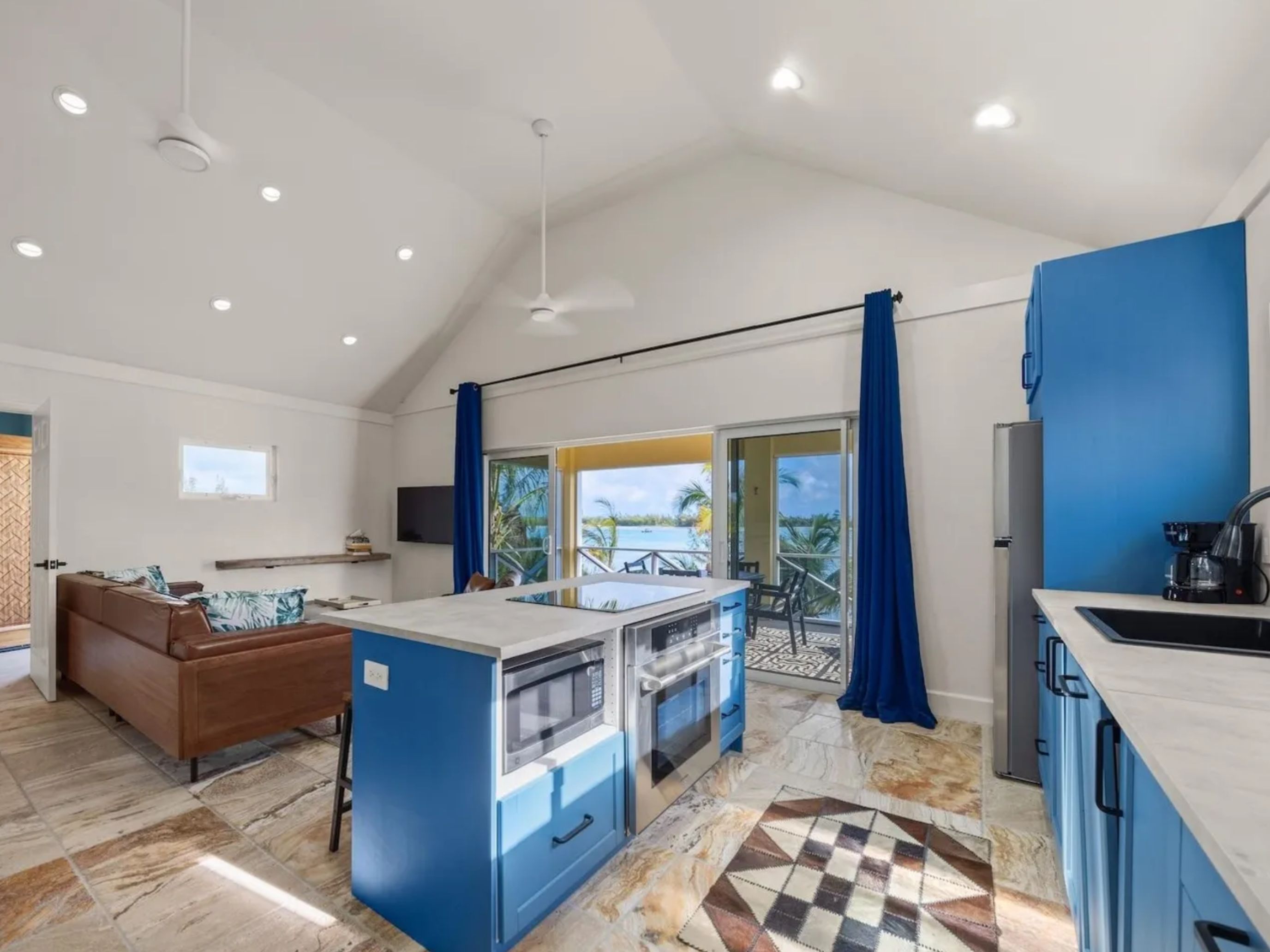 A modern kitchen with a central island, a dining area with a brown sofa, and a view of a pool through a sliding glass door.