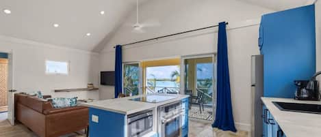 Una cocina moderna con una isla central, un área de comedor con sofá marrón y vistas a una piscina a través de una puerta corredera de vidrio.