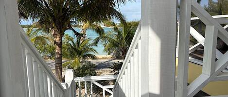A white wooden staircase leading to a balcony overlooking a beach with palm trees and a view of the ocean.