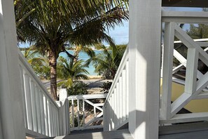 A white wooden staircase leading to a balcony overlooking a beach with palm trees and a view of the ocean.