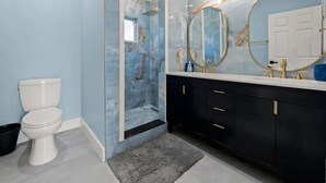A bathroom with a white toilet, a black vanity with gold fixtures, and a large mirror with a gold frame. - Lo key cottages-The Penthouse (green turtle cay)