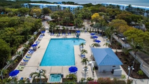 A resort with a large swimming pool surrounded by lounge chairs and umbrellas, a small pool, and a building with a blue roof. - Reel Large END Unit in Ocean Pointe Suites - Newly Renovated! (Tavernier)