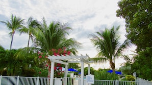 A gated entrance with a white pergola, surrounded by lush greenery and palm trees. - Reel Large END Unit in Ocean Pointe Suites - Newly Renovated! (Tavernier)