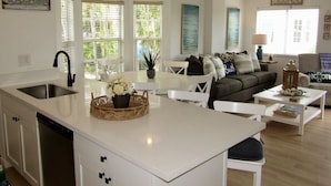 A modern kitchen with a central island, white cabinetry, and a dining area with a white table and chairs. - Reel Large END Unit in Ocean Pointe Suites - Newly Renovated! (Tavernier)