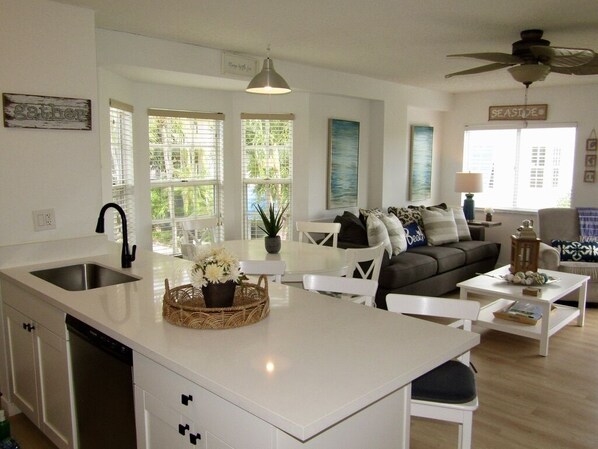 A modern kitchen with a central island, white cabinetry, and a dining area with a white table and chairs. - Reel Large END Unit in Ocean Pointe Suites - Newly Renovated! (Tavernier)
