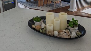 Et moderne køkken med marmorbordplade, et spiseområde med et træbord og stole, samt en hyggelig siddekrog med en blå sofa.