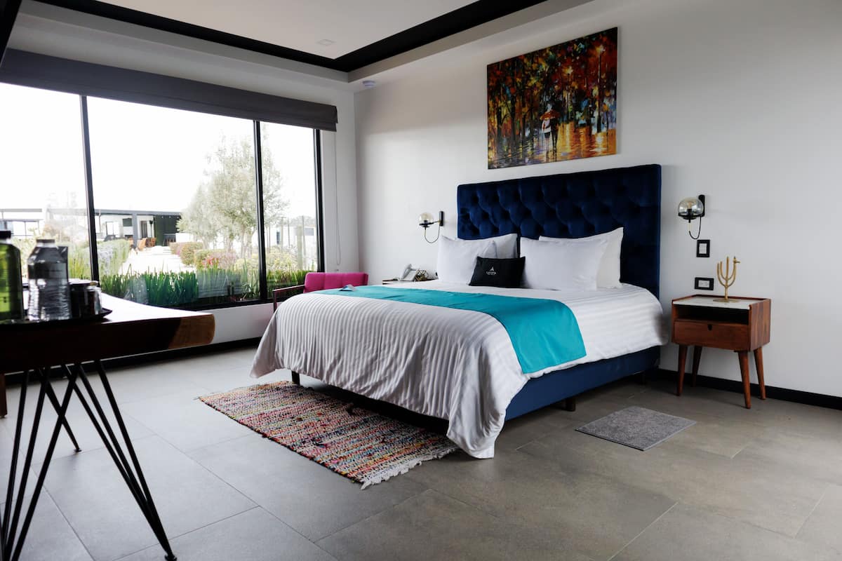 A modern bedroom with a large bed, a desk, and a window overlooking a garden.