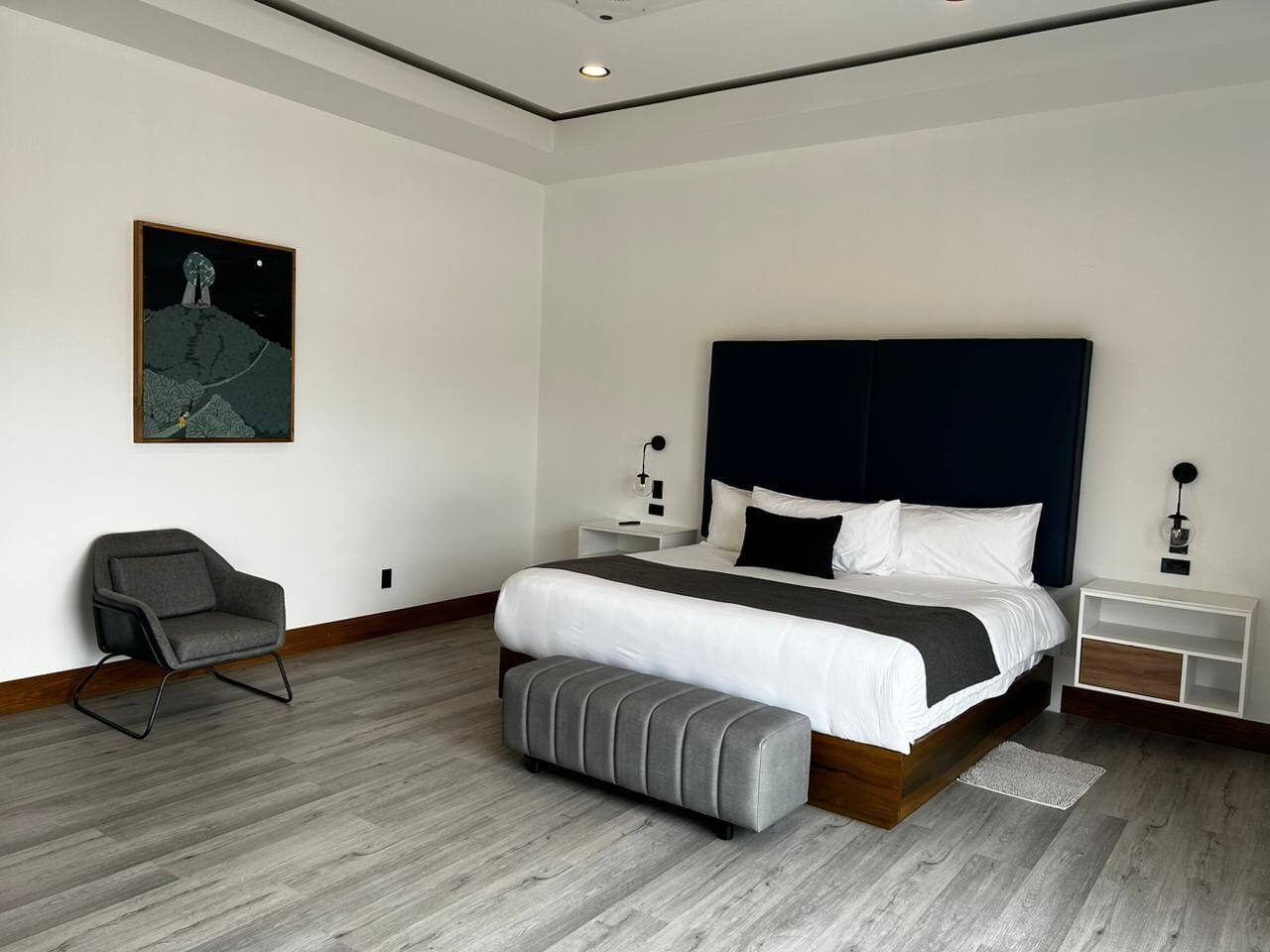 Un dormitorio moderno con una cama grande, una mesita de noche, una silla y una mesita auxiliar.