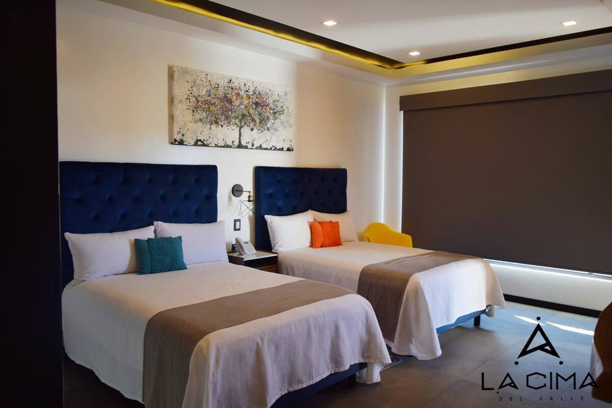 A hotel room with two beds, a large window, and a painting on the wall.