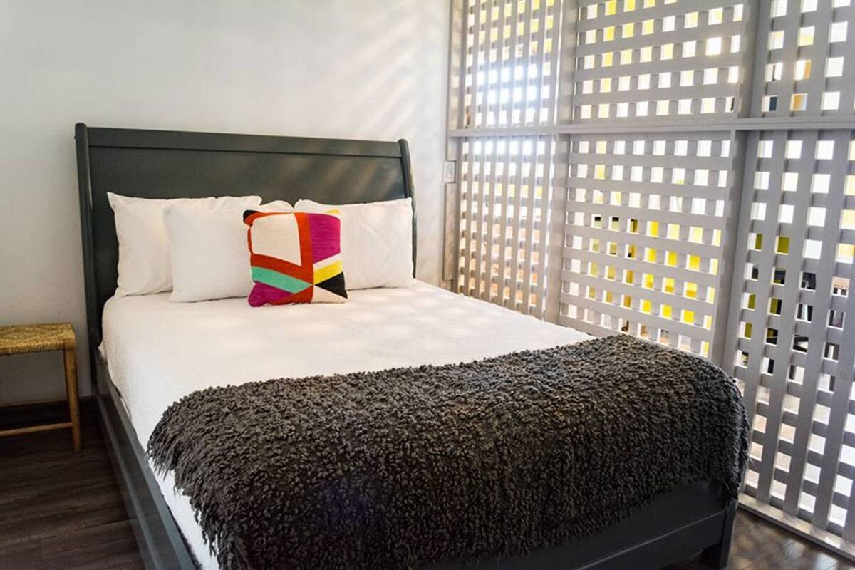 A bed with a dark headboard, white pillows, a colorful pillow, and a dark blanket.