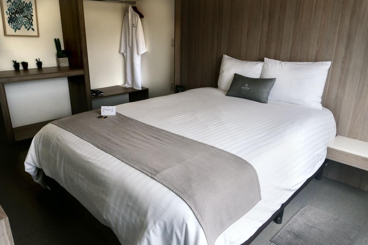 A neatly made bed with a grey throw blanket, a bedside table with a lamp, and a small card on the bed.