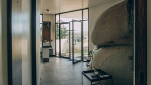Un interior moderno con una escultura de piedra, una puerta de vidrio que da al exterior y una pequeña mesa con una planta.