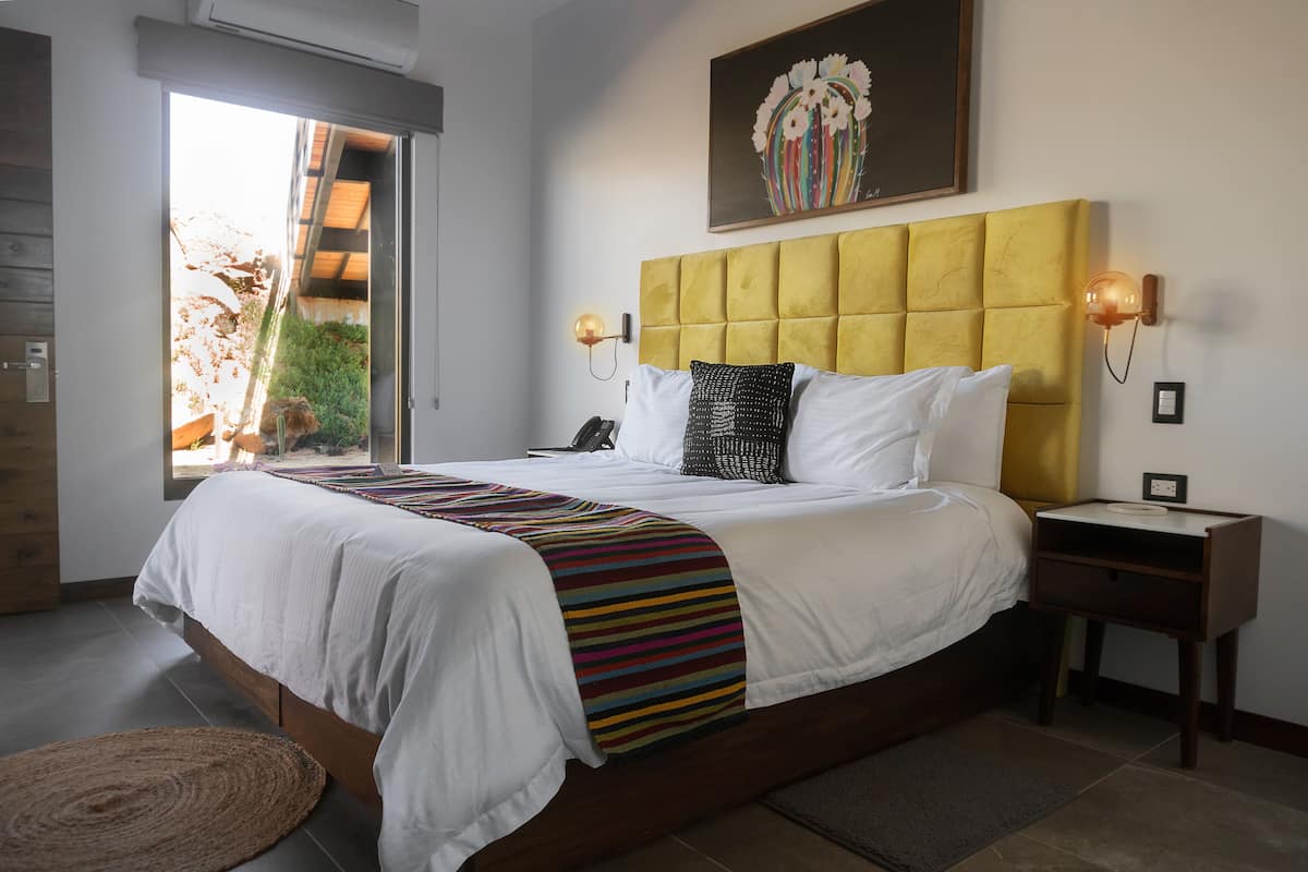 A bedroom with a large bed, a headboard, bedside tables, a nightstand, a wall-mounted lamp, and a painting.