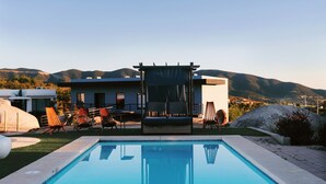 Un área de piscina moderna con vistas despejadas del paisaje circundante, incluyendo colinas y un edificio al fondo.