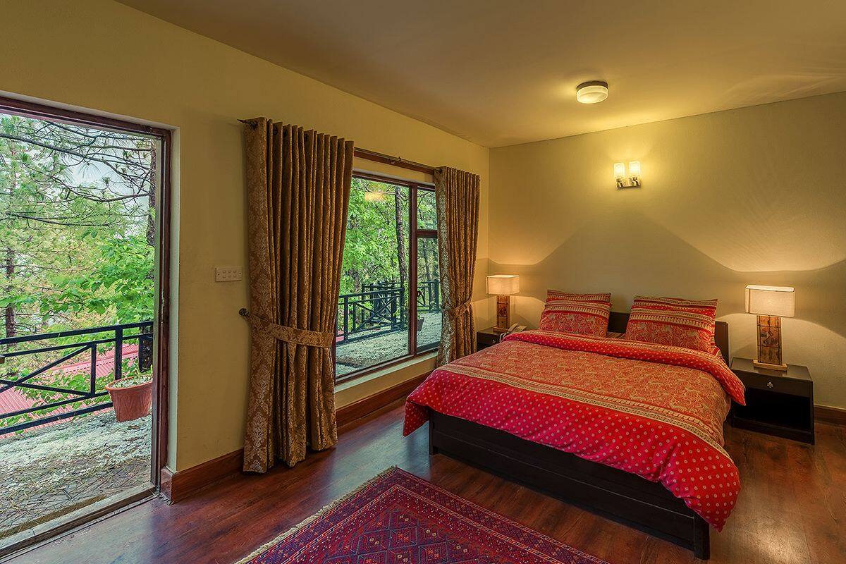 Un dormitorio con una cama grande, dos lámparas de noche, una ventana con cortinas y vistas a zonas verdes.