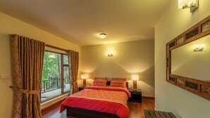 Un dormitorio con una cama grande, dos lámparas de noche, un banco de madera y vistas al exterior a través de una ventana con cortinas.
