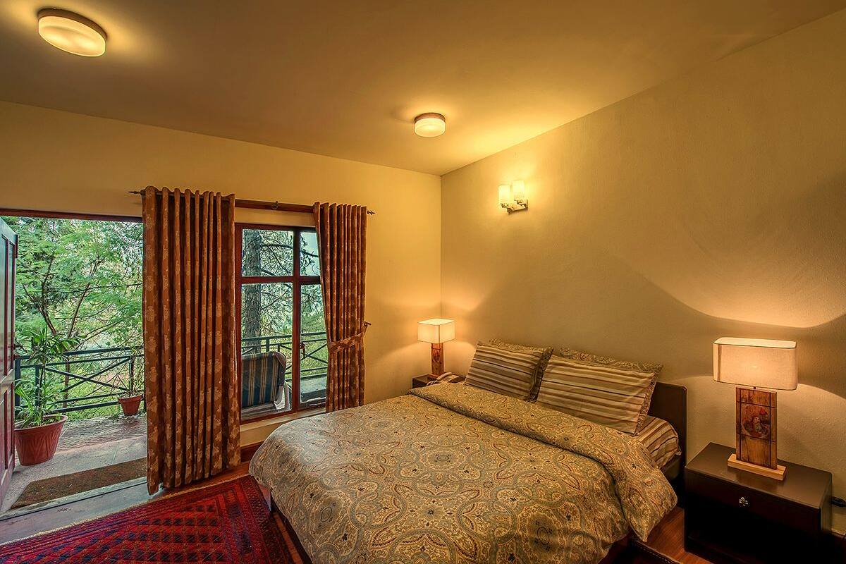 Un dormitorio con una cama grande, dos lámparas de noche, una ventana con cortinas y vistas a zonas verdes.