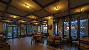 Un comedor espacioso con grandes ventanales, mesas y sillas de madera.