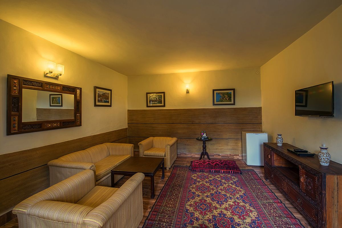 Una sala de estar con un sofá, un sillón, una mesa de centro y un televisor. Hay luces fijadas a la pared y cuadros enmarcados.