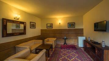 Una sala de estar con un sofá, un sillón, una mesa de centro y un televisor. Hay luces fijadas a la pared y cuadros enmarcados.