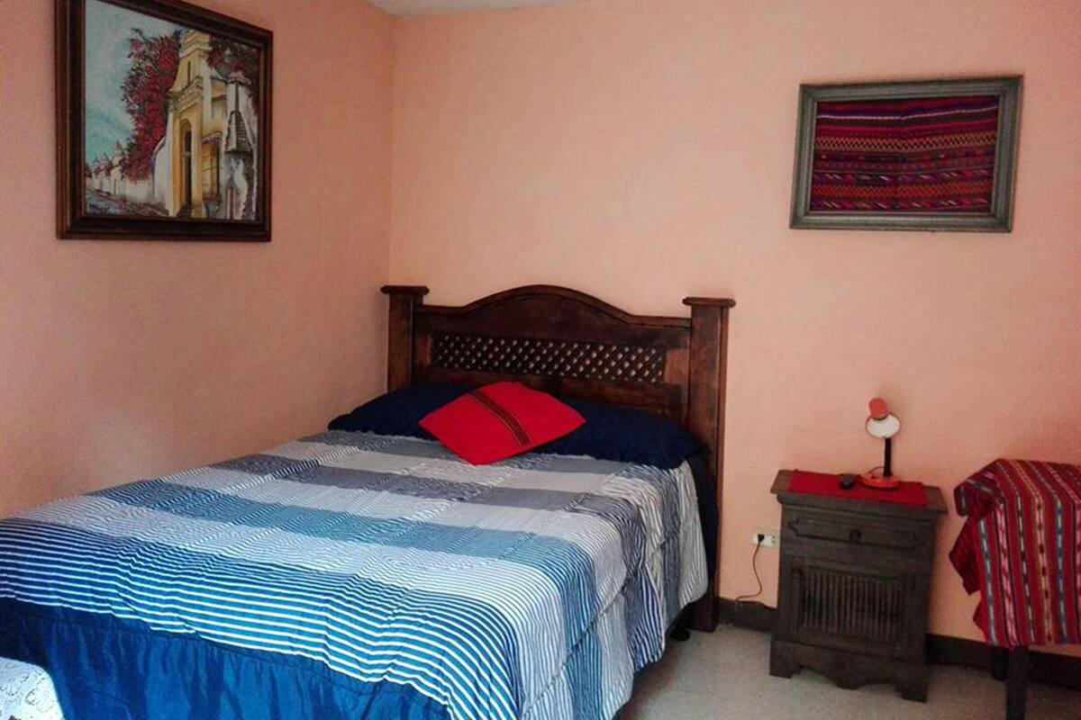 A bedroom with a wooden bed, a nightstand, a lamp, and two framed pictures on the walls.