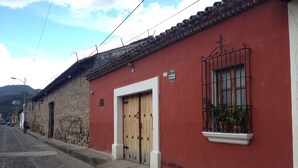 A red building with a wooden door and a window with a metal grill. - Casa de Leon (Antigua Guatemala)