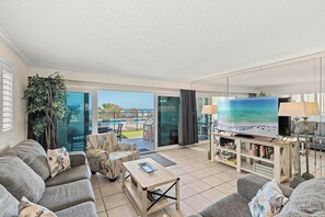 Un salon spacieux doté d’un grand téléviseur, de sièges confortables, d’une table basse et offrant une vue sur une piscine et un espace extérieur.