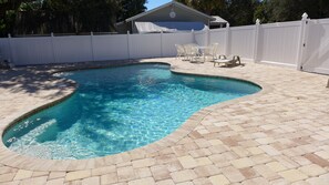A swimming pool with a curved edge, surrounded by a paved patio and a white fence. -  Trick or Treat: Spooktacular Halloween Deals! (Fort Myers)
