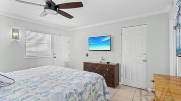 A bedroom with a bed, a ceiling fan, a dresser, a door, and a TV on the wall.
