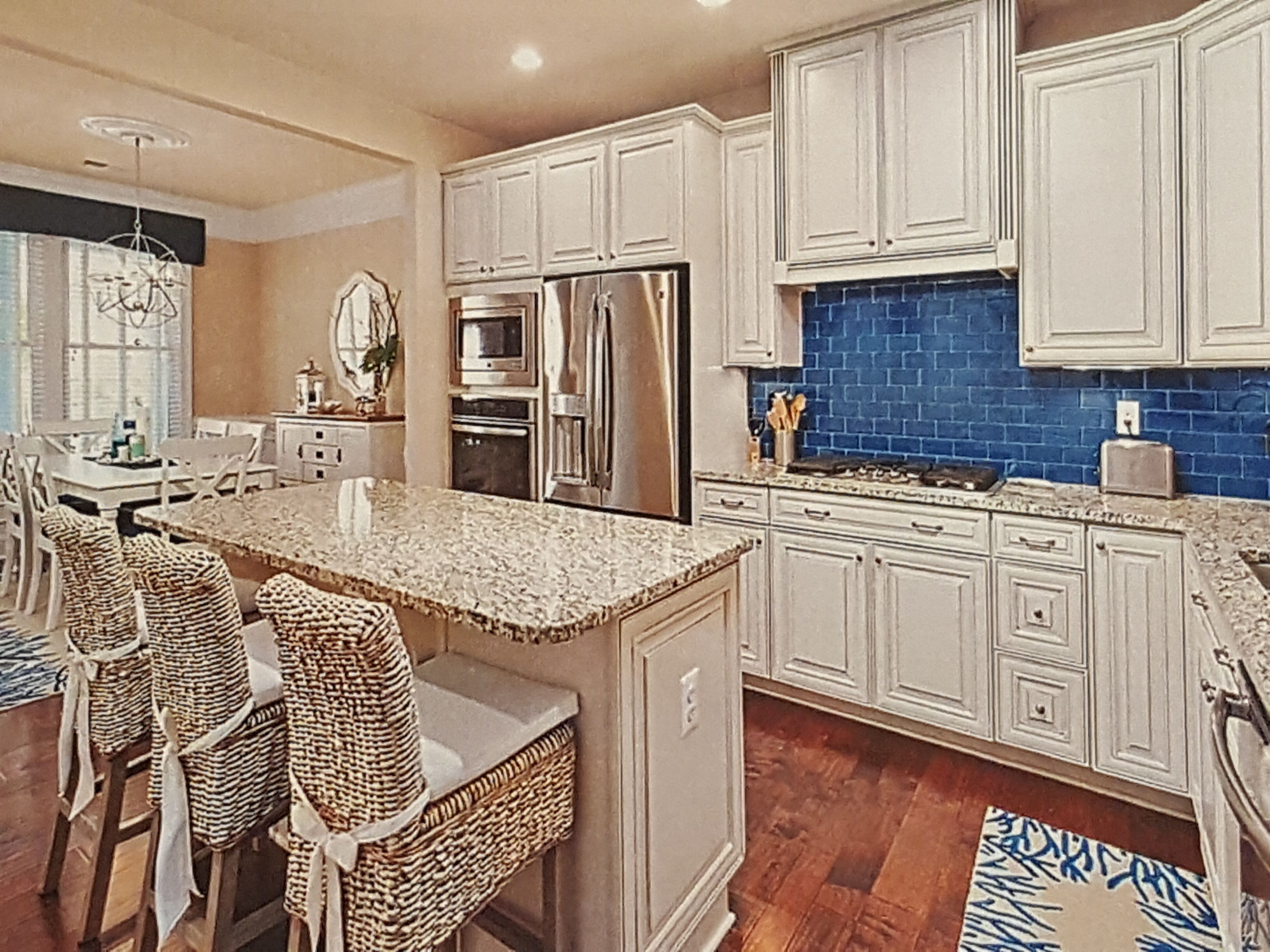 A kitchen with white cabinets, a blue backsplash, and a central island with chairs.