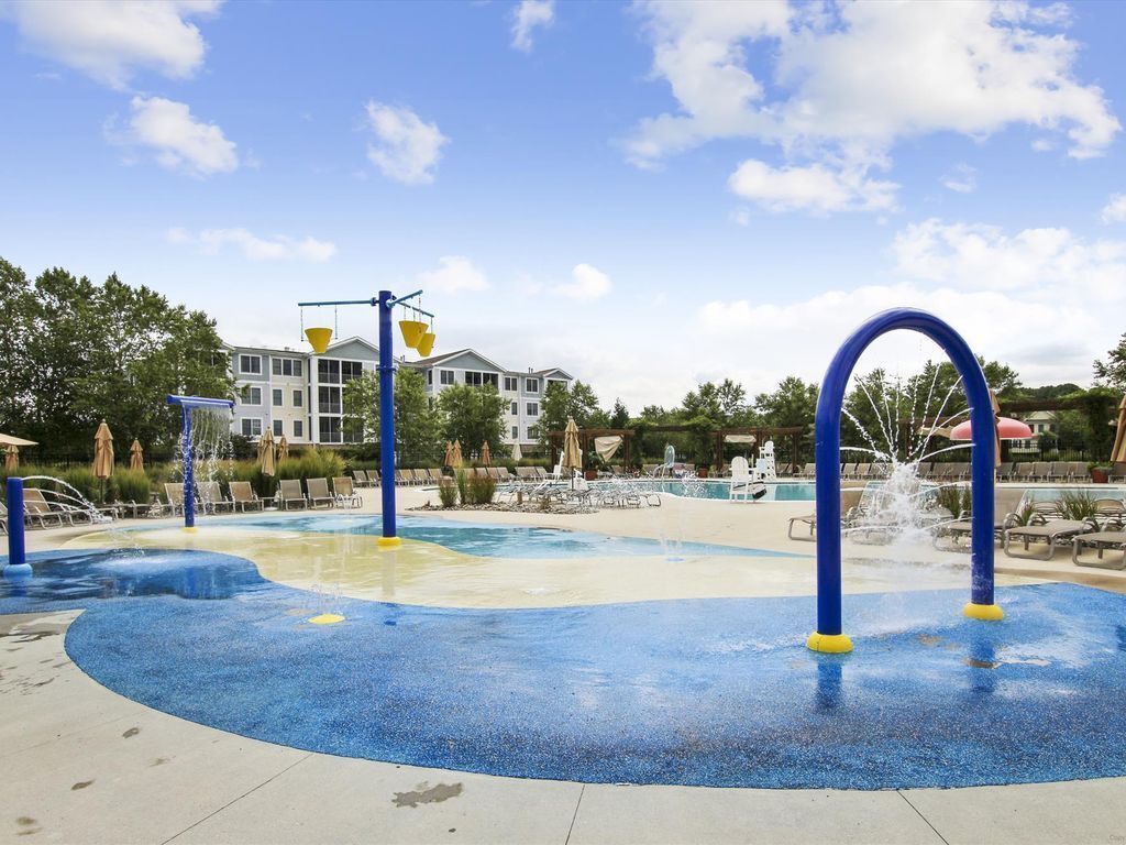 A water play area with blue and yellow safety surfacing, a pool, and lounge chairs.