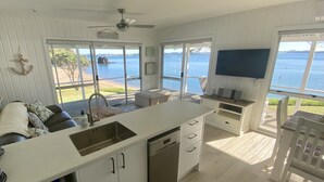 A modern kitchen with a large island, a dining area with a view of the sea, and a cozy seating area. - Beachfront Escape - Tapeka Beach Bach (Tapeka Point (Russell))