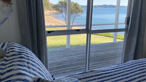 A room with a large window overlooking a beach and water. - Beachfront Escape - Tapeka Beach Bach (Tapeka Point (Russell))