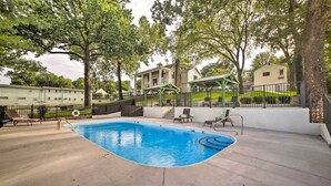 A swimming pool with a curved edge, surrounded by a concrete deck. There are lounge chairs and a covered seating area. - Steps to Branson Landing: Cozy Downtown Cottage! (Branson)