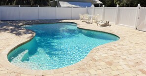 A swimming pool with a curved edge, surrounded by a white fence and a patio area with chairs and a table. - Halloween Deal: Spooky Good Savings! (Fort Myers)