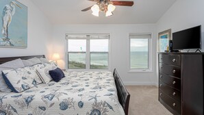 A bedroom with a bed, a dresser, a ceiling fan, and two windows with views of the ocean. - Spacious condo with sleeping loft - Sleeps 10 on Pensacola Bay - San Deluna 29 (Pensacola Beach)