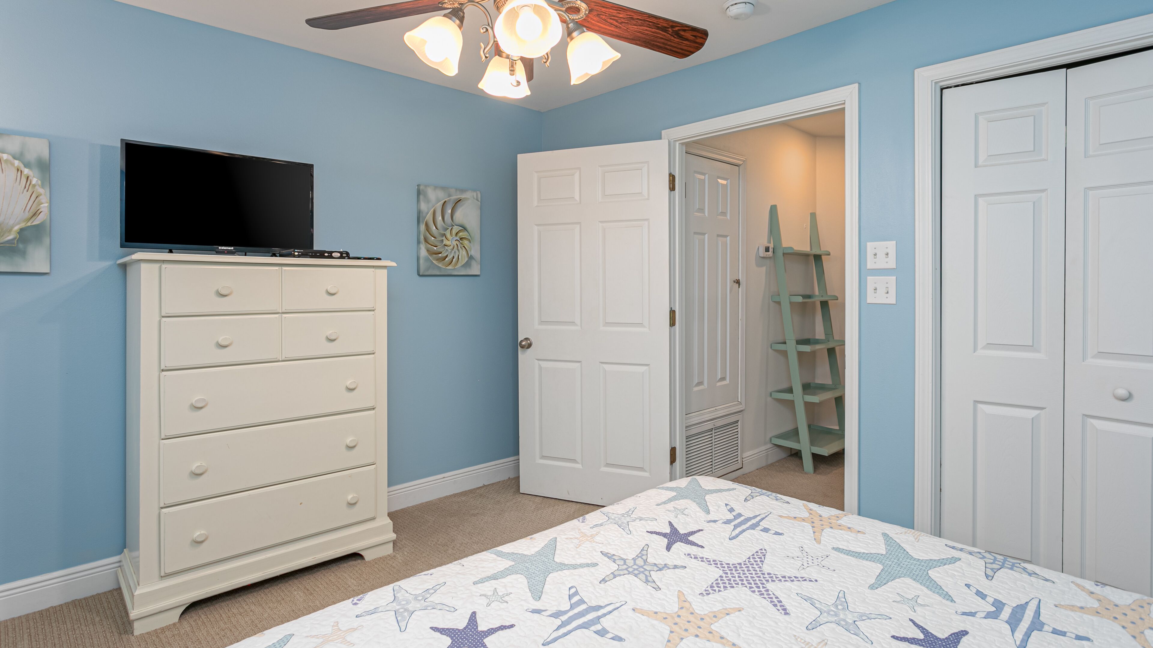 Un dormitorio con cama, cómoda, ventilador de techo y una puerta que da a otra habitación.