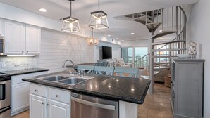 A modern kitchen with a central island, stainless steel appliances, and a dining area with a view. - Spacious condo with sleeping loft - Sleeps 10 on Pensacola Bay - San Deluna 29 (Pensacola Beach)