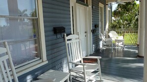 Een veranda met witte schommelstoelen, een tafel, een brievenbus en een deur.