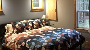 A bedroom with a large bed, wooden ceiling beams, a window with a view of trees, and a wall-mounted light fixture. - Couples Retreat, NEW Hot Tub 2022, ORV, Right From the Front Door (Baldwin)