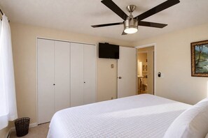 Habitación de hotel con cama, ventilador de techo, televisor montado en la pared y puerta que da a un baño.