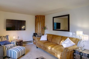 Una sala de estar con un sofá de cuero, un sillón a rayas, un reposapiés, un mueble de madera, un espejo grande y un televisor de pantalla plana.