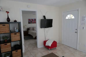 A room with a bed, a red chair, a television mounted on the wall, and a door with a window.